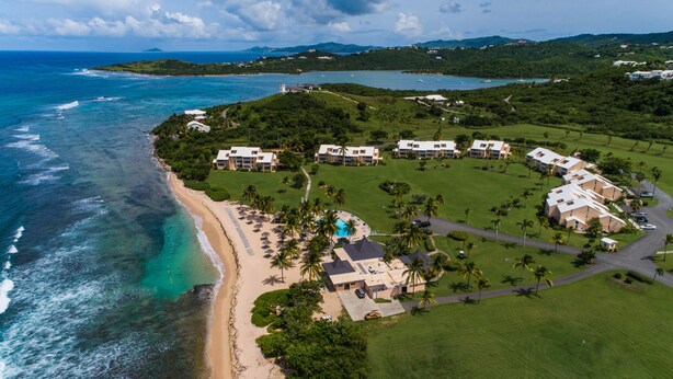 Vista aerea di un resort con proprietà sulla spiaggia, una piscina e vegetazione lussureggiante.