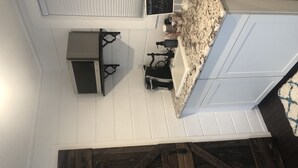 Una cocina con armarios blancos, encimera de granito y techo de madera oscura.