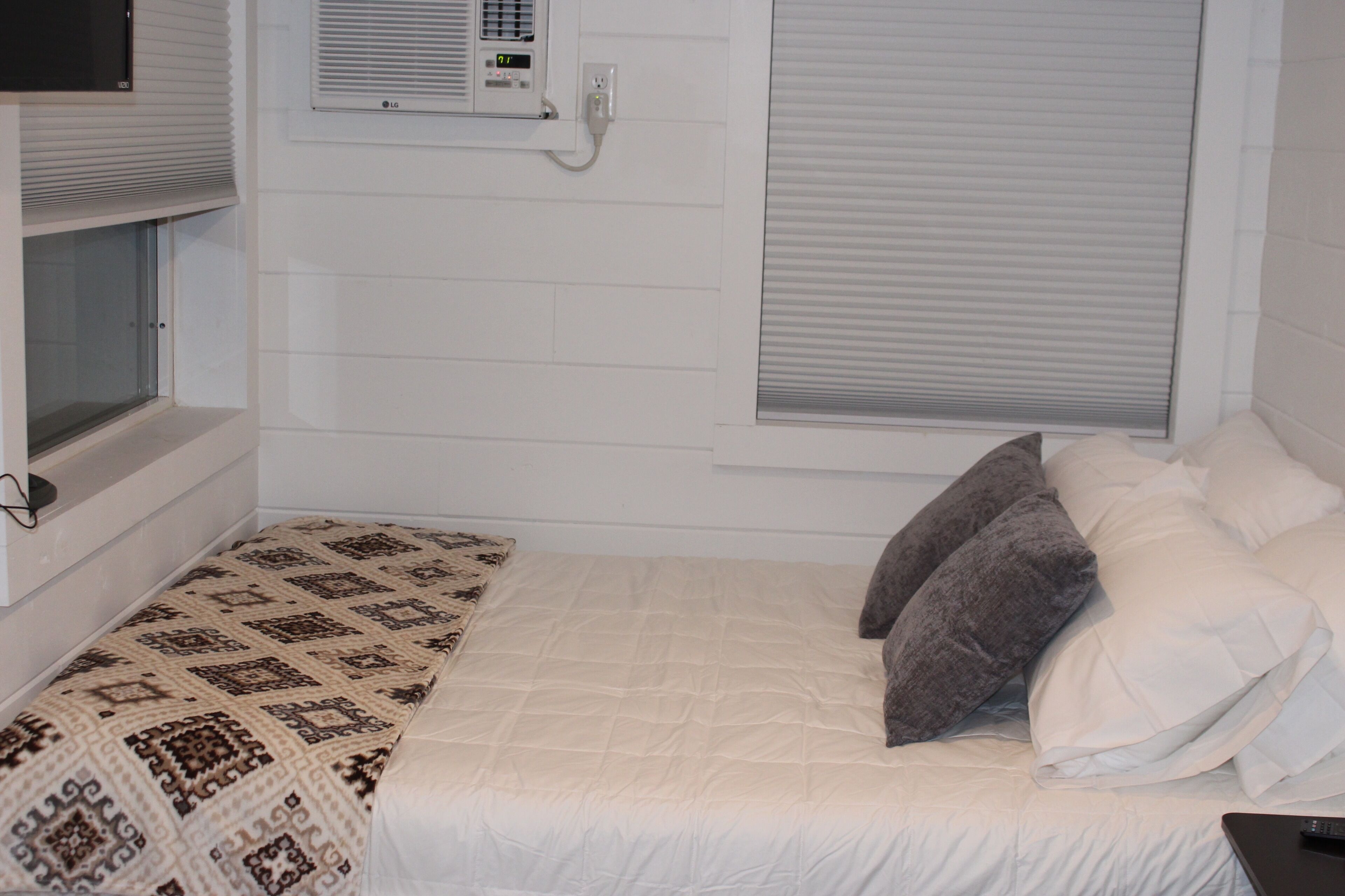 Una camera da letto con un letto, una finestra con tende, un condizionatore d'aria e una TV a parete.