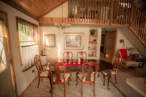 Une salle à manger avec une table et des chaises en bois, un lustre et des œuvres d’art encadrées accrochées aux murs.