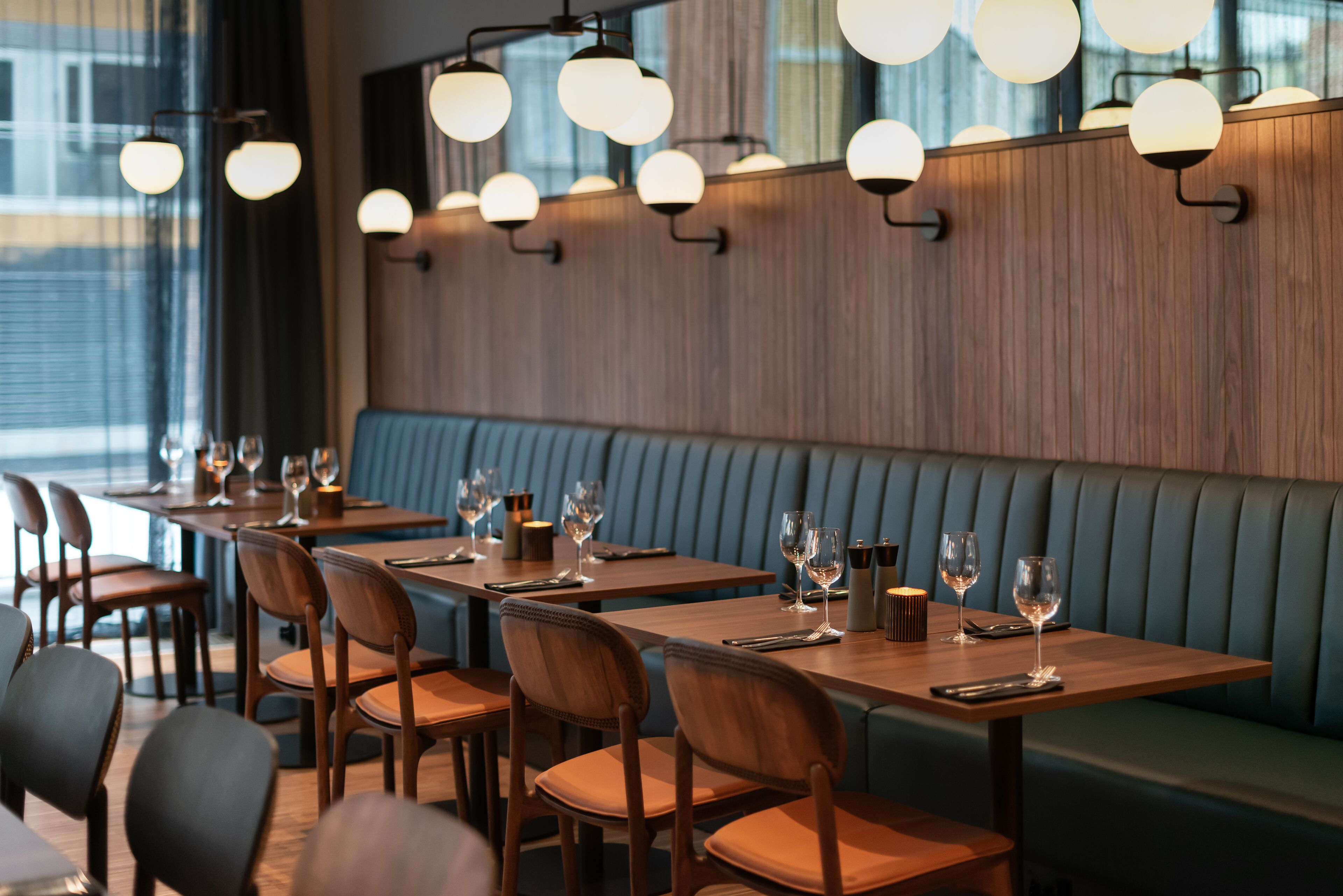 A restaurant interior with wooden tables and chairs, a blue cushioned bench, and pendant lighting.