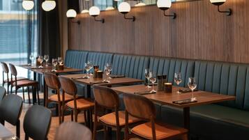A restaurant interior with wooden tables and chairs, a blue cushioned bench, and pendant lighting.