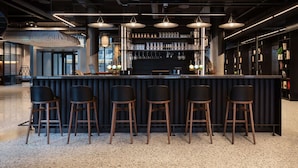 Zona de bar moderna con mostrador, taburetes e iluminación colgante.