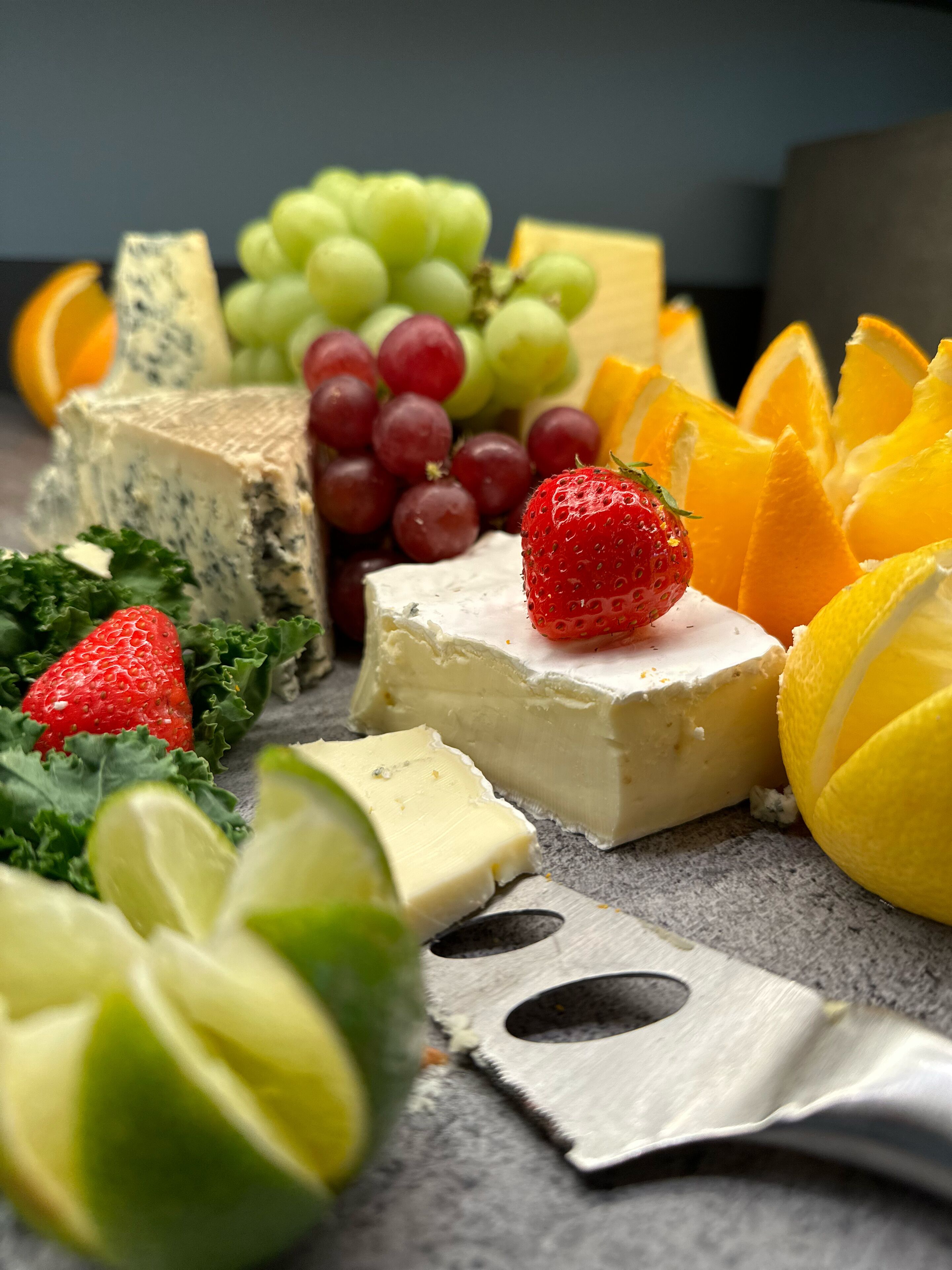 A variety of cheeses, fruits, and a cutting board on a table.