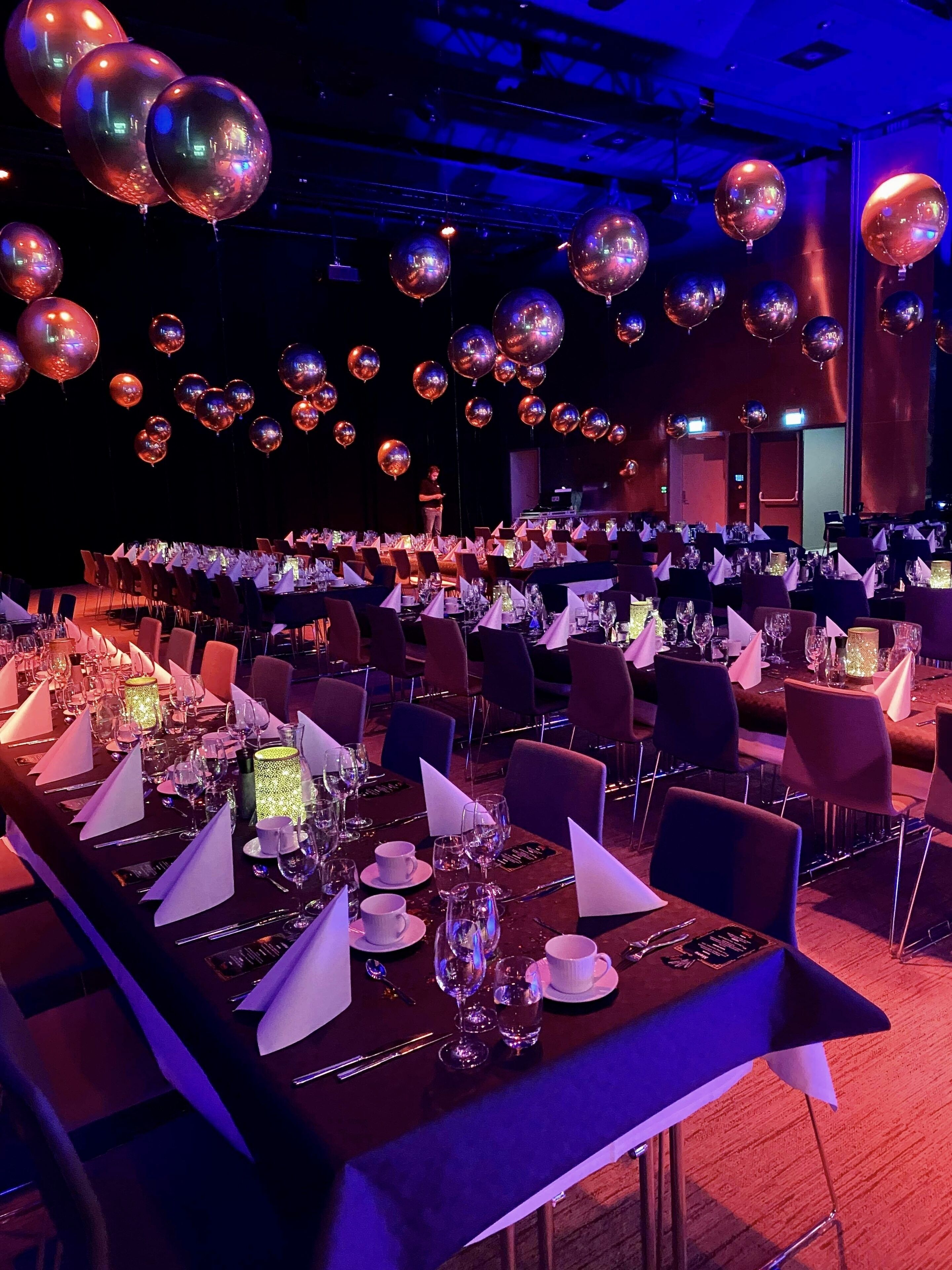 A banquet hall with tables set for a formal event, featuring reflective disco balls and ambient lighting.