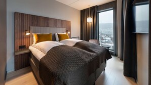 Una habitación de hotel moderna con una cama grande, vistas a la ciudad y un cabecero de madera.