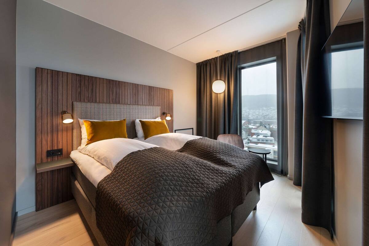 A modern hotel room with a large bed, a view of the city, and a wooden headboard.