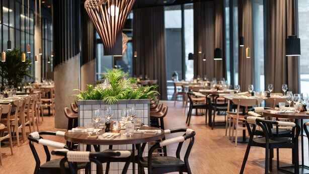 Un interior de restaurante moderno con mesas redondas, sillas oscuras y lámparas colgantes.