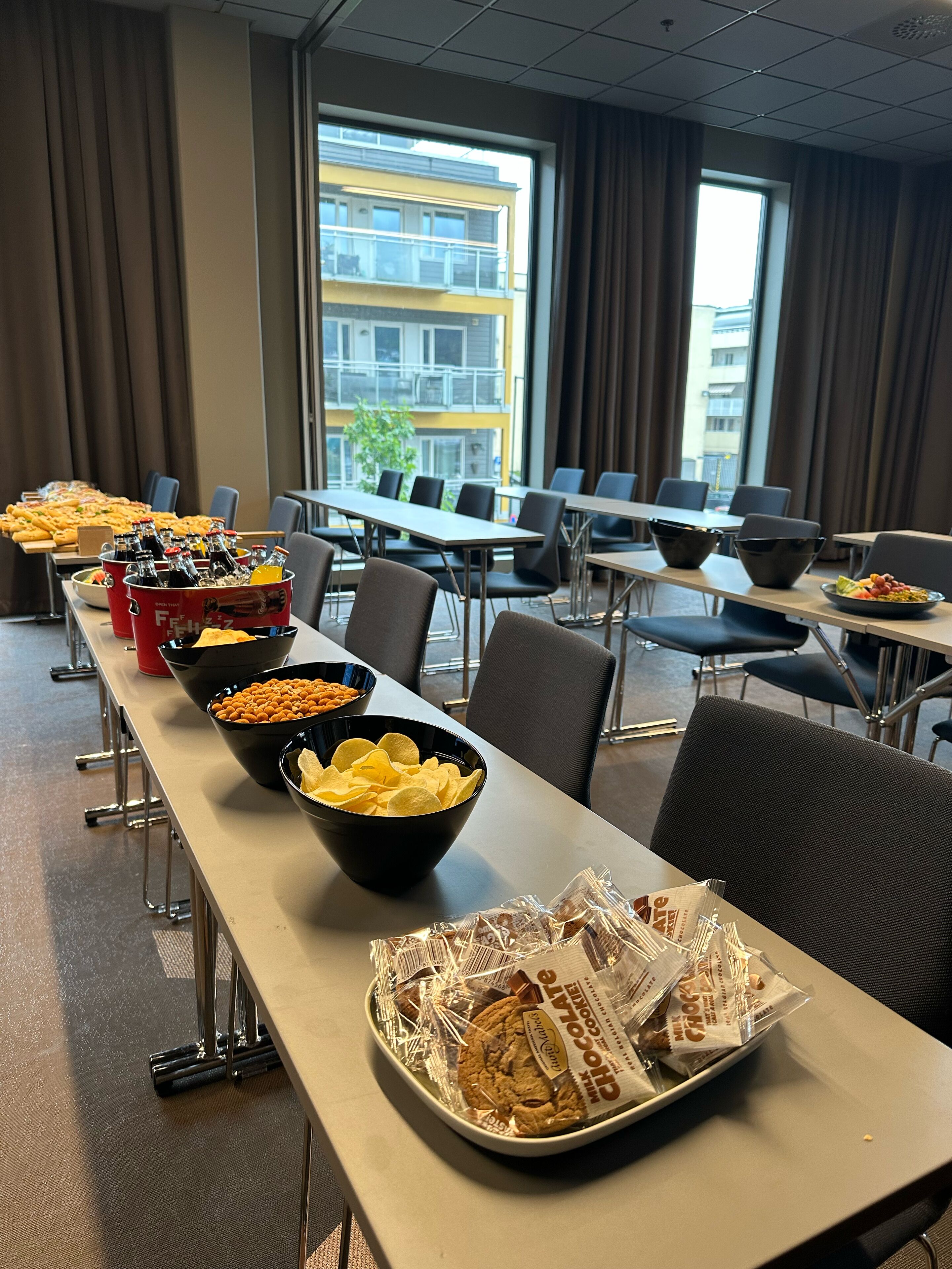 A conference room with a long table set for a meeting, equipped with chairs and a view of a building through large windows.