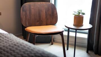Una habitación moderna con una silla de madera, una mesita con una planta en maceta y vistas al exterior a través de una ventana.