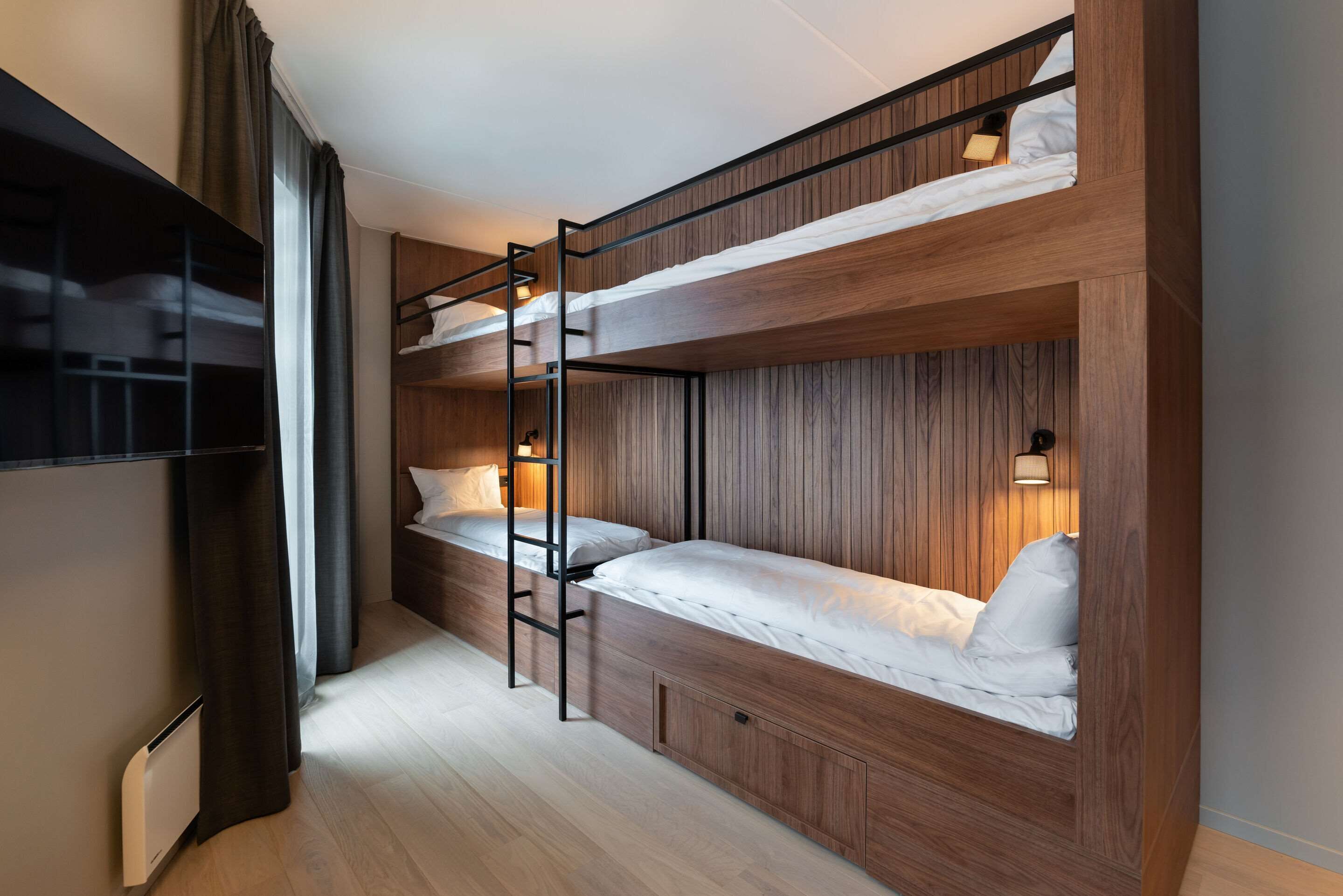A bunk bed room with a ladder, wooden paneling, and a TV on the left.
