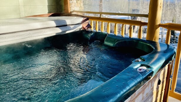 Un jacuzzi con una terraza de madera y una pared de piedra al fondo.