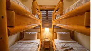 Una habitación con dos literas de madera, una mesita de noche con lámpara y una ventana con persianas.