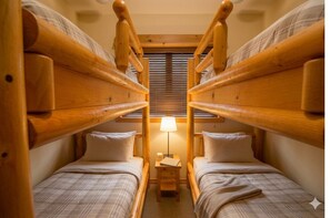 A room with two wooden bunk beds, a small bedside table with a lamp, and a window with blinds.