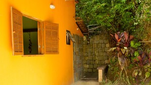 Un sendero estrecho conduce a una entrada de muro de piedra, flanqueado por un edificio amarillo brillante con contraventanas y un ventanal pequeño.