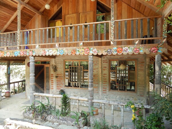A wooden house with a balcony, stone walls, and potted plants. - Dogs and Fish Dream Land (Baños de Agua Santa)