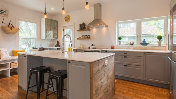 Una cocina moderna con una isla central, taburetes de bar y un amplio ventanal que proporciona luz natural.
