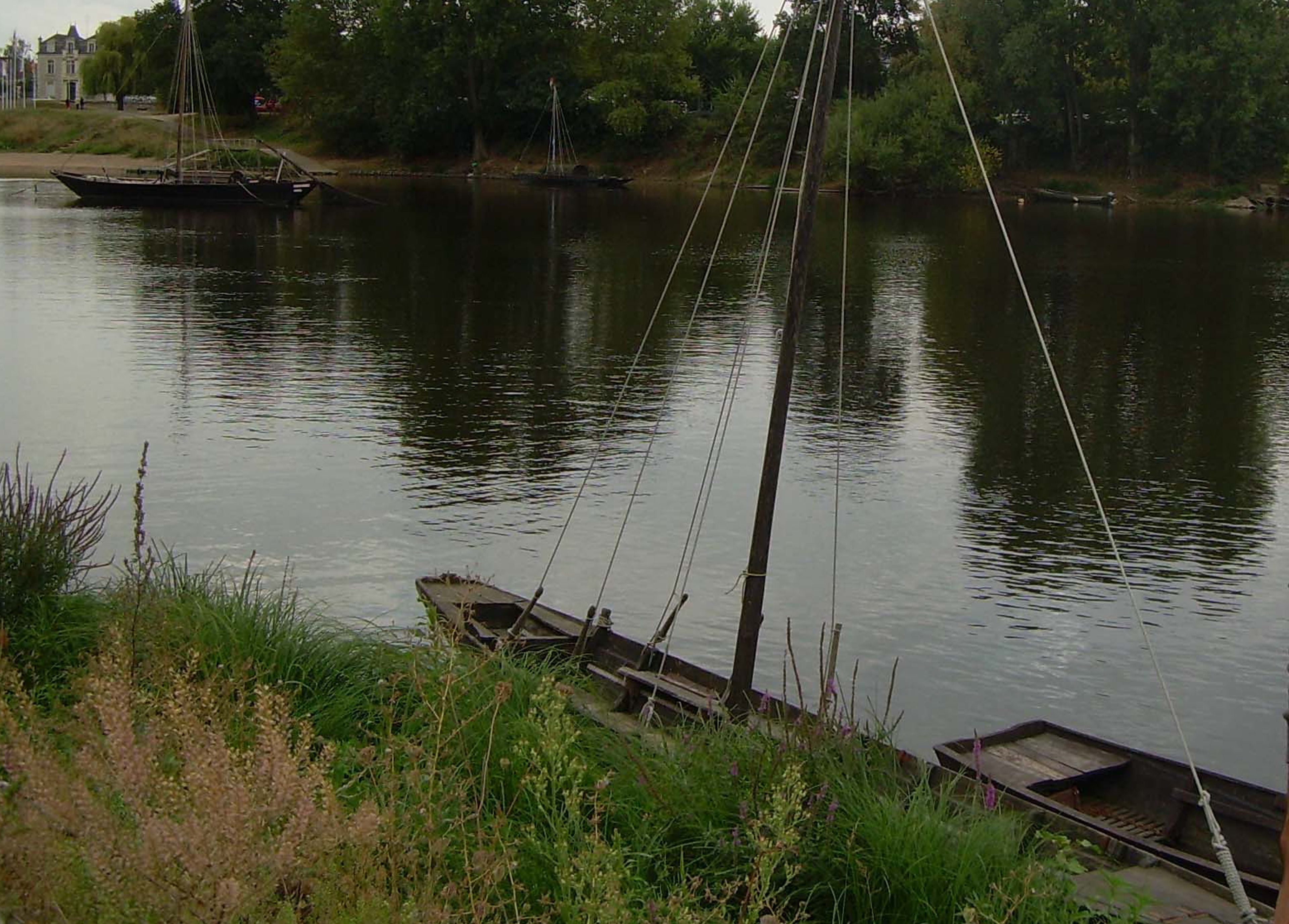 A calm river with boats docked along the shore, surrounded by greenery and trees.
