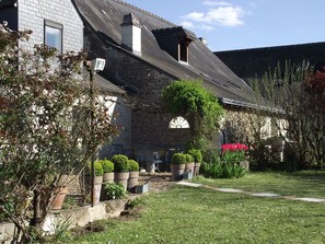 Ein Haus aus Stein mit einem geneigten Dach, einem kleinen Fenster und einem Garten mit Topfpflanzen und einem Weg.