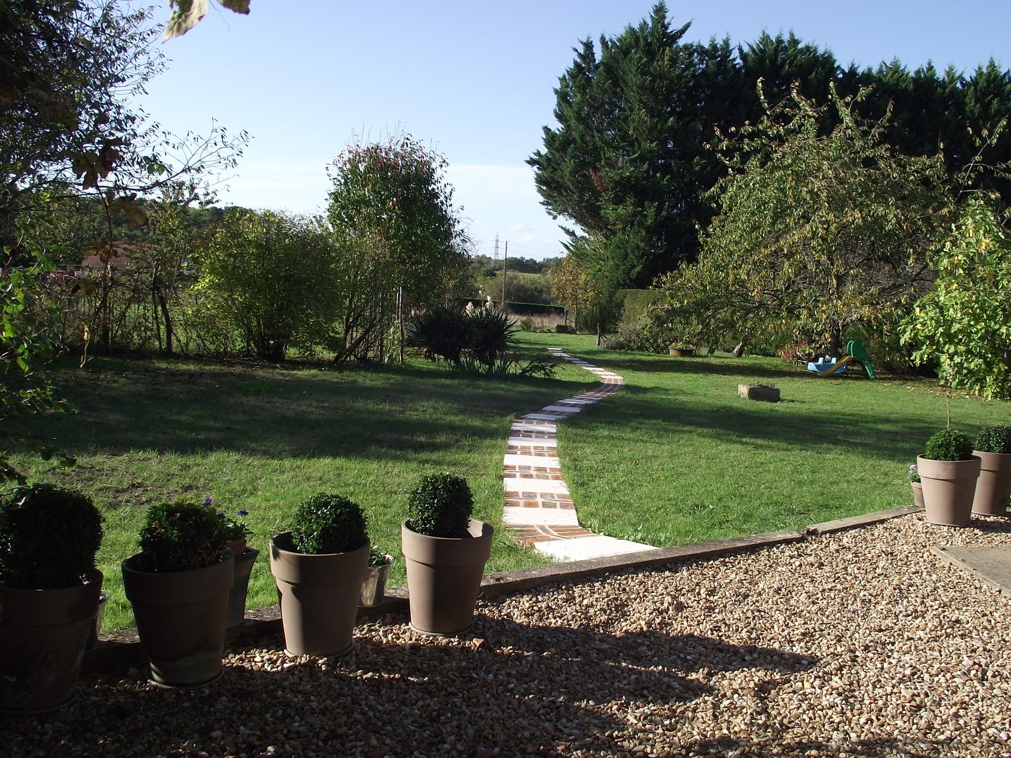 A garden pathway leading through a well-maintained lawn with potted plants and trees.