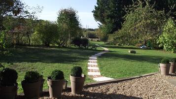 A garden pathway leading through a well-maintained lawn with potted plants and trees.
