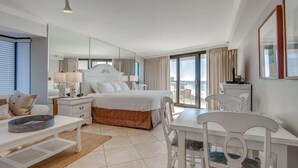 Habitación de hotel con una cama grande, un escritorio, una silla, una mesa de comedor y un balcón con cortinas.