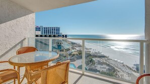 Un balcón con mobiliario de mimbre que da a una playa y un edificio de hotel.