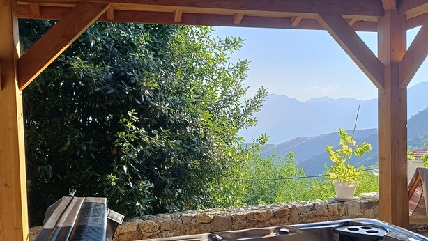 Un bain à remous sous une pergola en bois, avec vue sur les montagnes et la verdure.