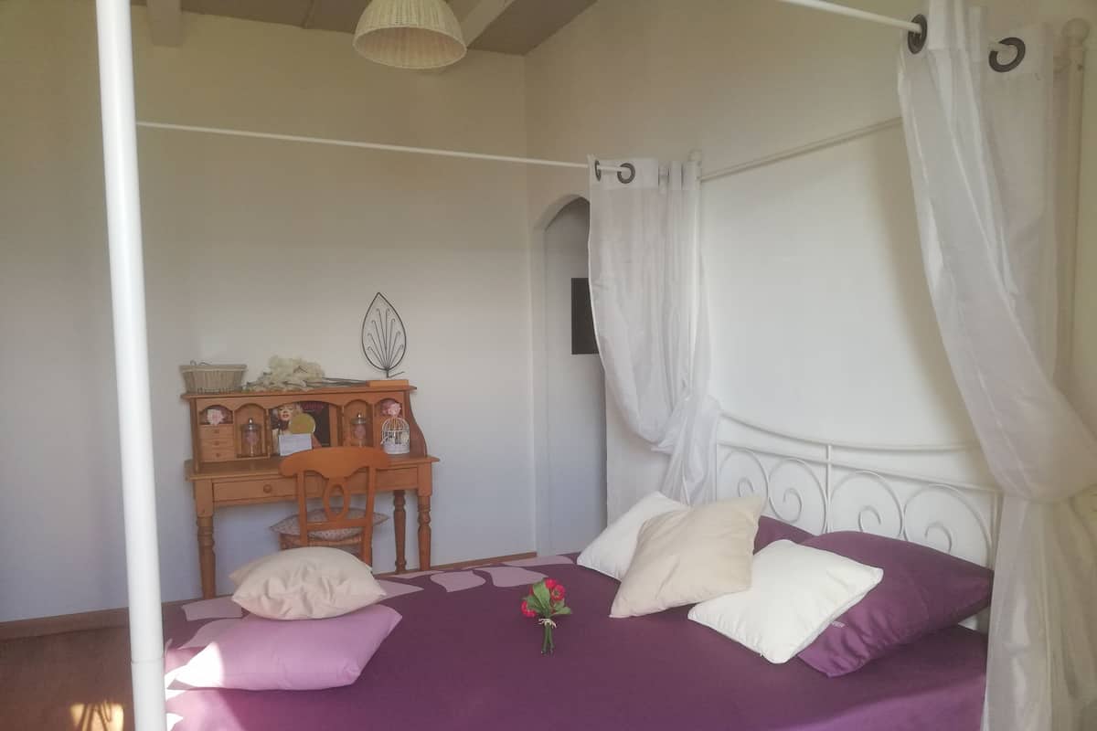 Een bed met hemelbed, een houten bureau met stoel, en een decoratief object aan de muur.