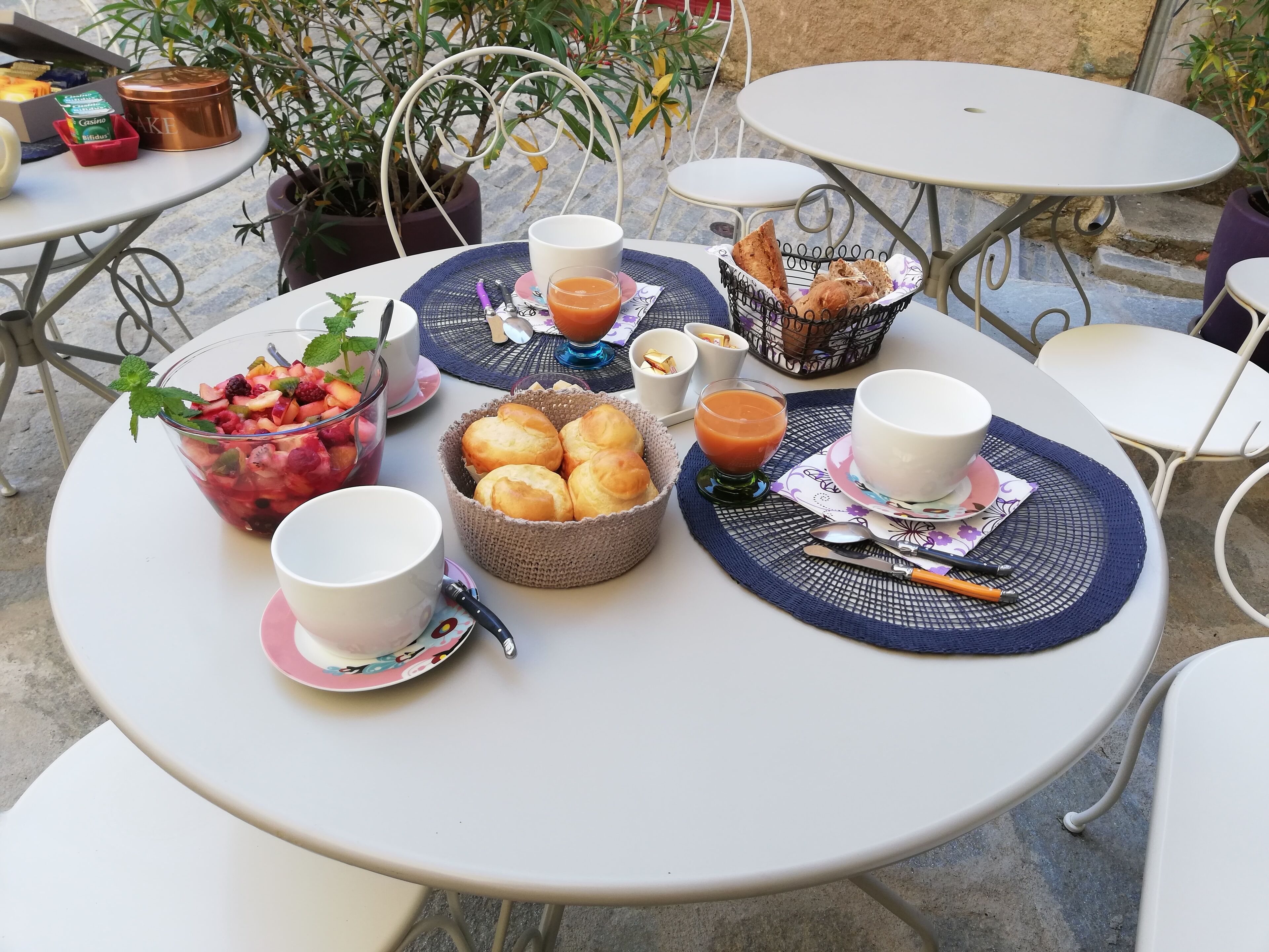 Una mesa redonda dispuesta con alimentos para el desayuno, incluyendo un frutero, pan y un vaso de zumo de naranja.