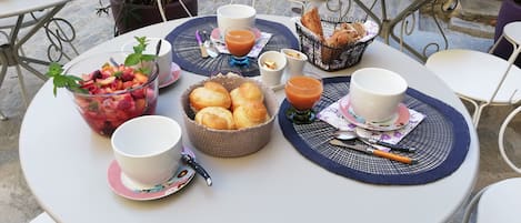 Una mesa redonda dispuesta con alimentos para el desayuno, incluyendo un frutero, pan y un vaso de zumo de naranja.