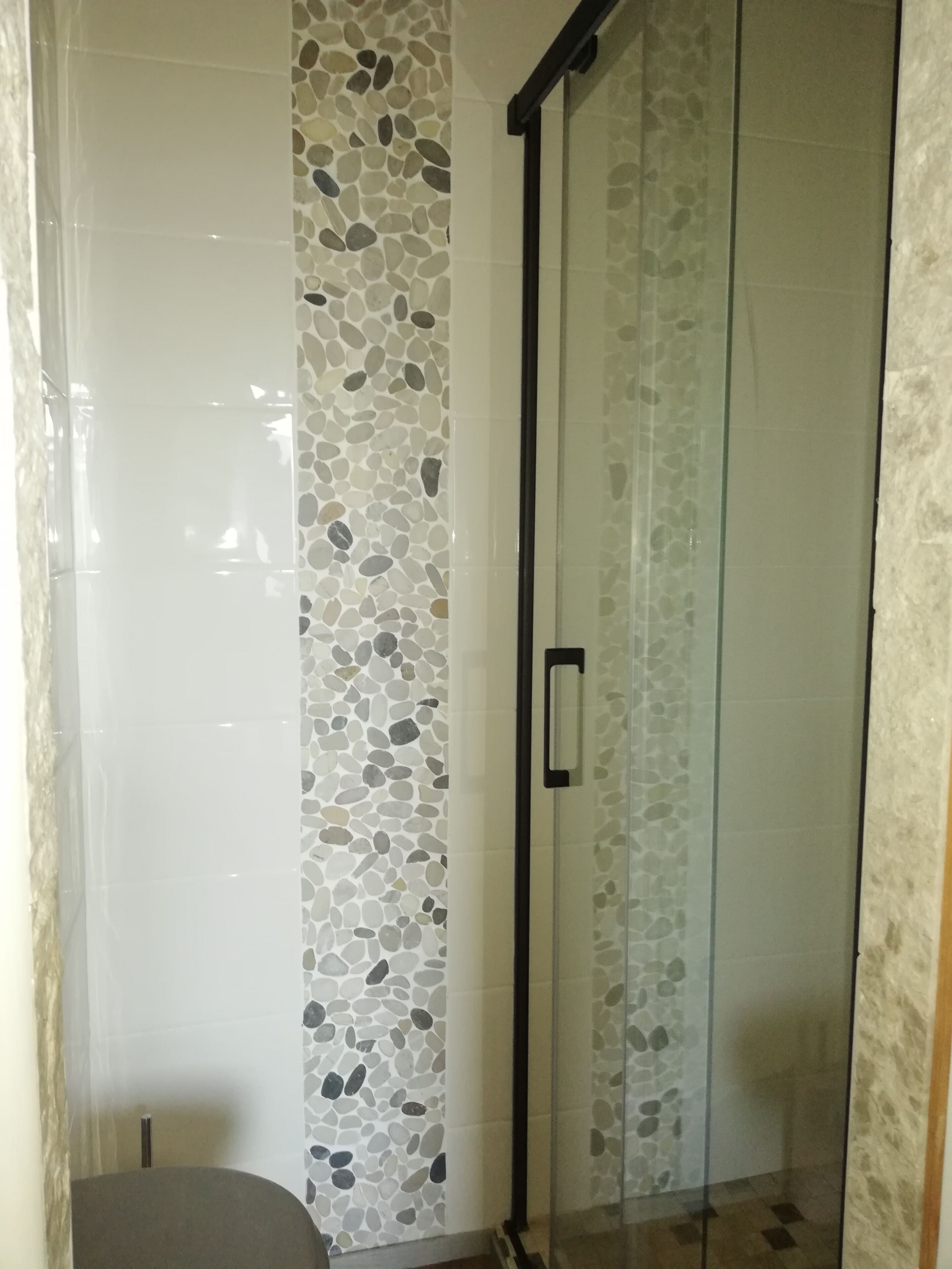 Ducha con paredes revestidas de un diseño de guijarros, protegida por un cerramiento de vidrio.