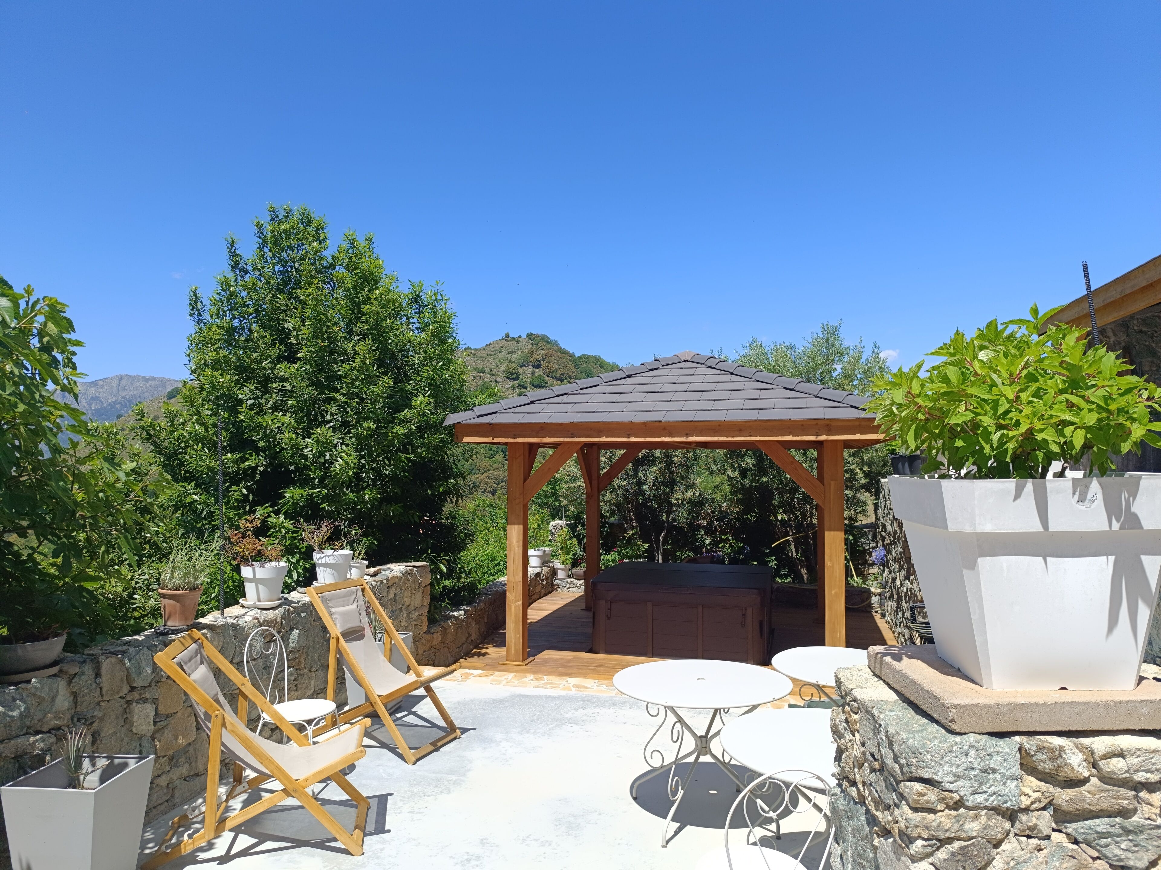 A patio with a wooden pergola, stone seating, and potted plants.
