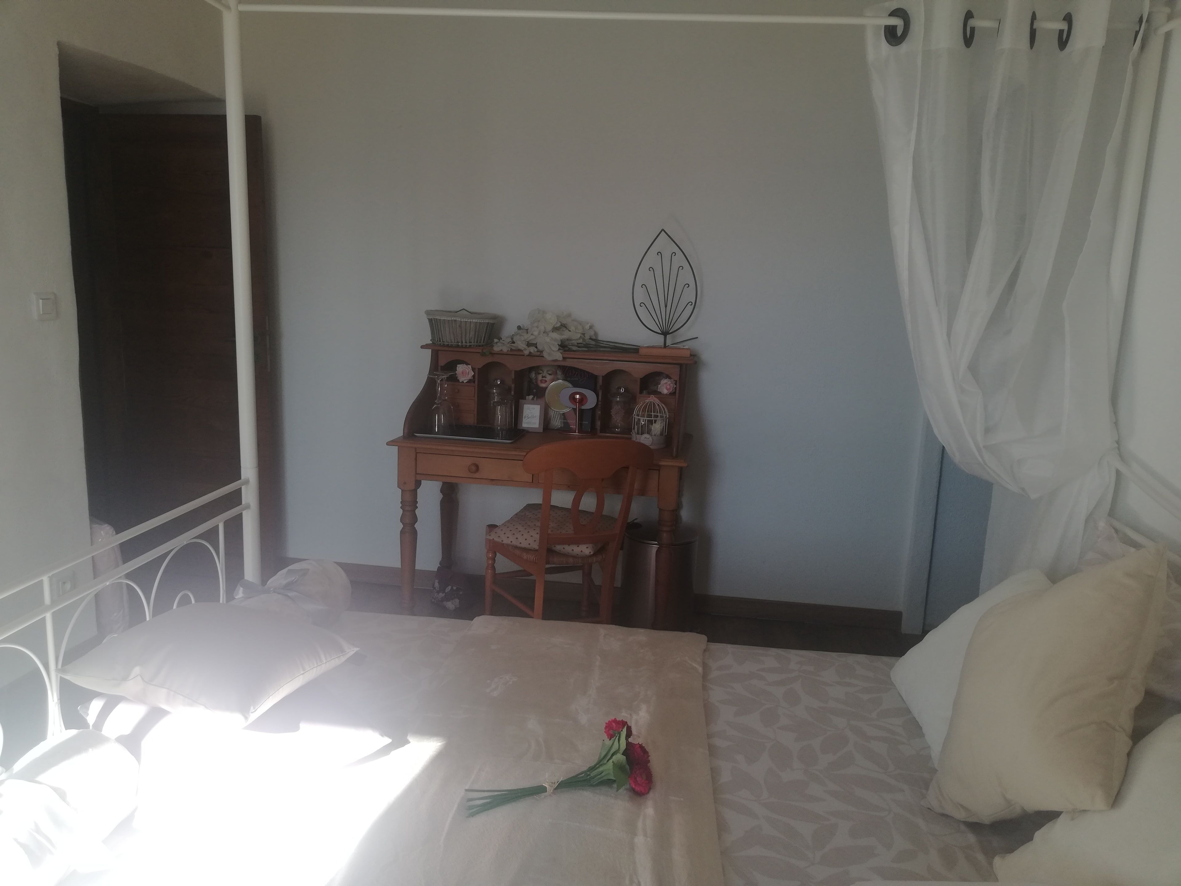 A bedroom with a bed, a desk with a chair, a window with curtains, and a bedside table with a lamp.