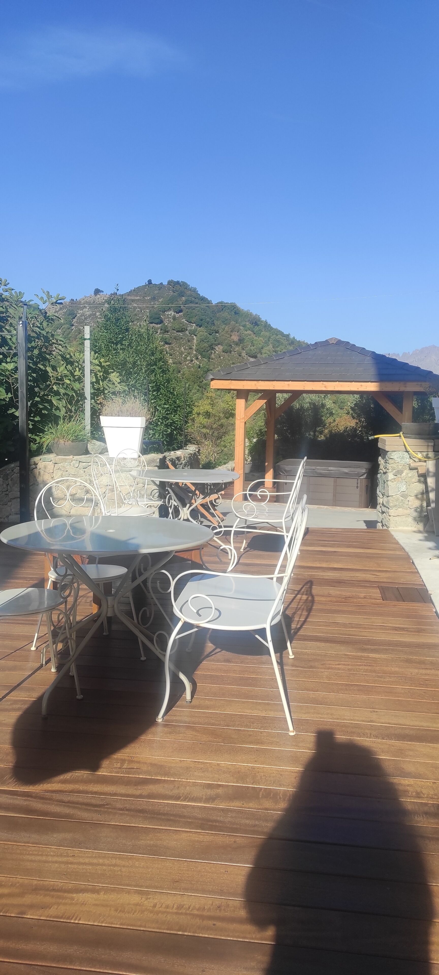 Un patio al aire libre con una mesa redonda y sillas, una pérgola y un muro de piedra.