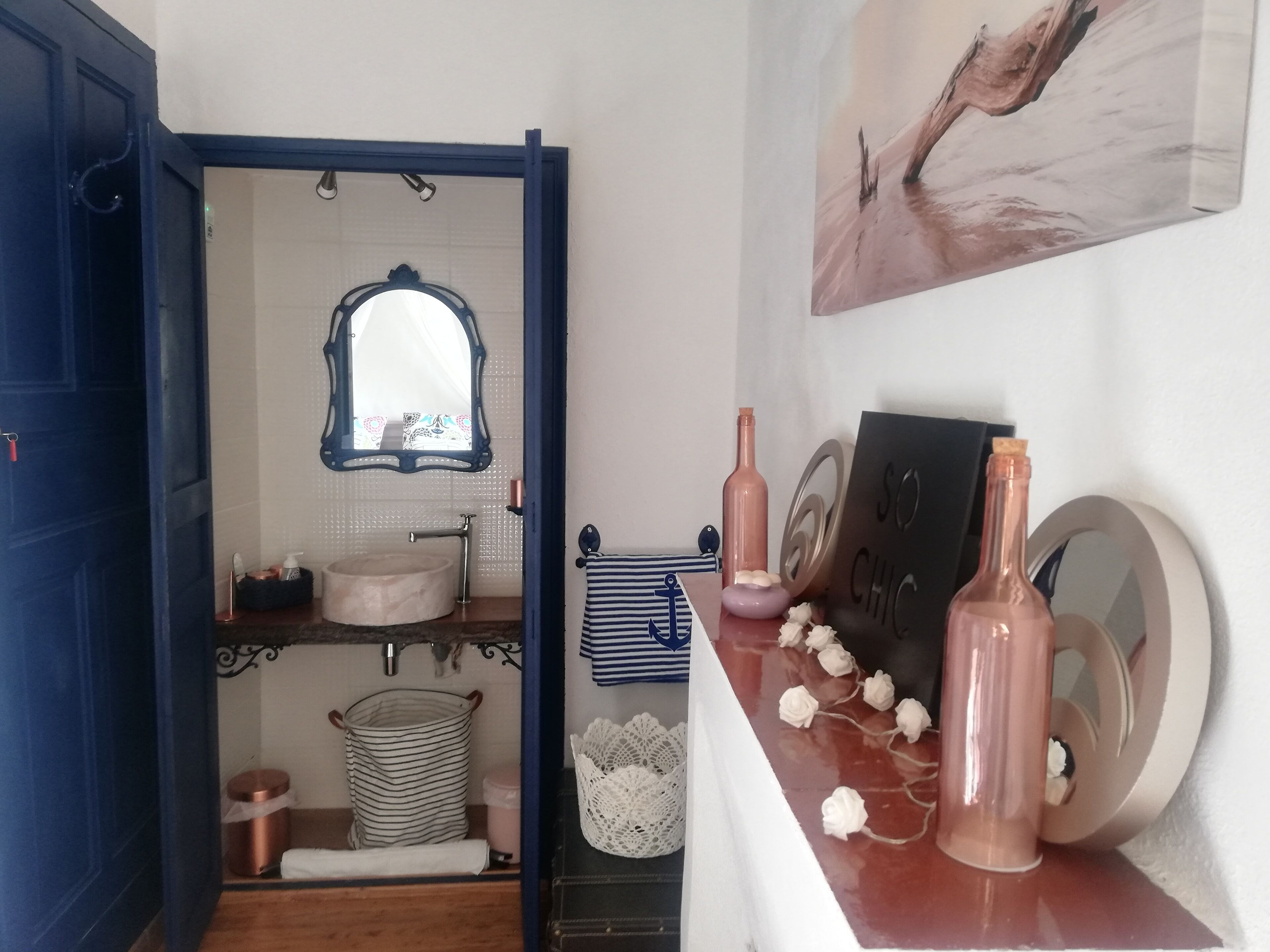 A bathroom with a blue door, a mirror, a sink, a towel rack, and decorative items on the counter.