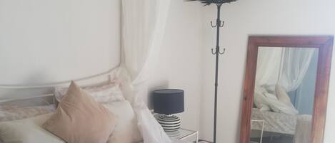 Ein ordentlich bezogenes Bett mit Baldachin, einer Nachttischlampe und einem Spiegel an der Wand.