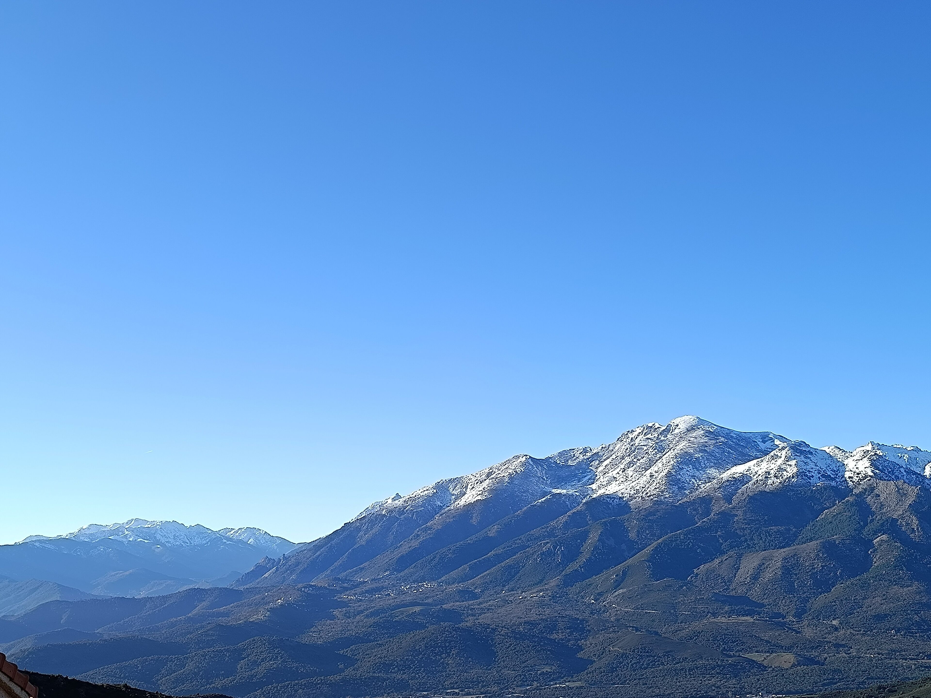 Een bergketen met besneeuwde toppen en een helderblauwe lucht.