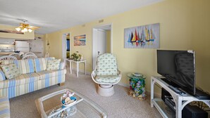 Un salon comprenant un canapé, un fauteuil, un téléviseur et un tableau représentant des voiliers.