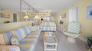 Un salon avec des canapés à rayures, une table basse en osier et un fauteuil orné d’un motif de palmier.