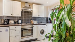 Una cocina moderna con armarios blancos, una estufa de acero inoxidable, horno empotrado y lavadora.