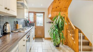 Una cocina con armarios de madera, un lavamanos y una estufa. Se ve una escalera con barandilla de madera que sube a un nivel superior.