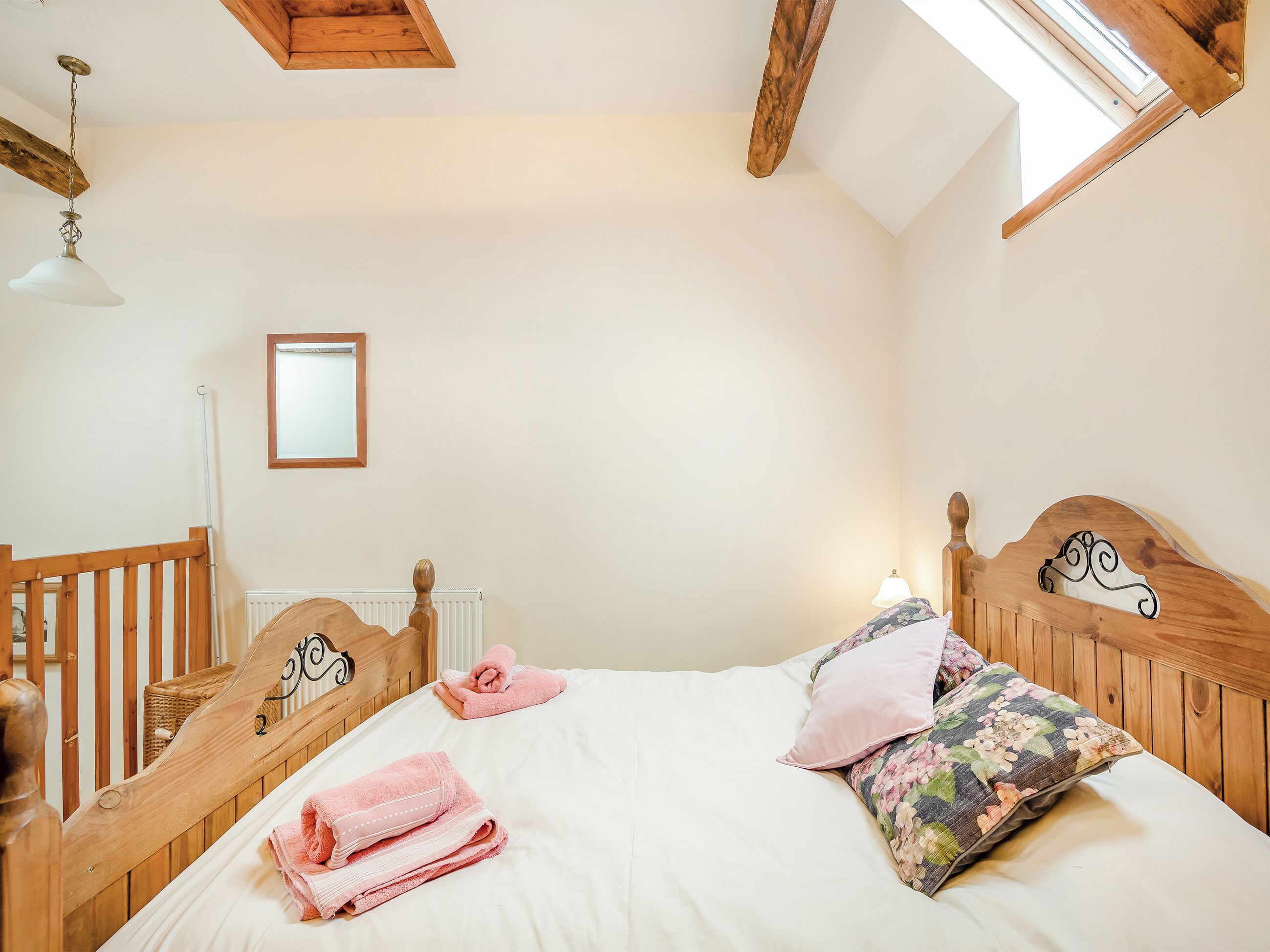A bedroom with a wooden headboard, a white bedspread, pink towels, and a floral pillow.