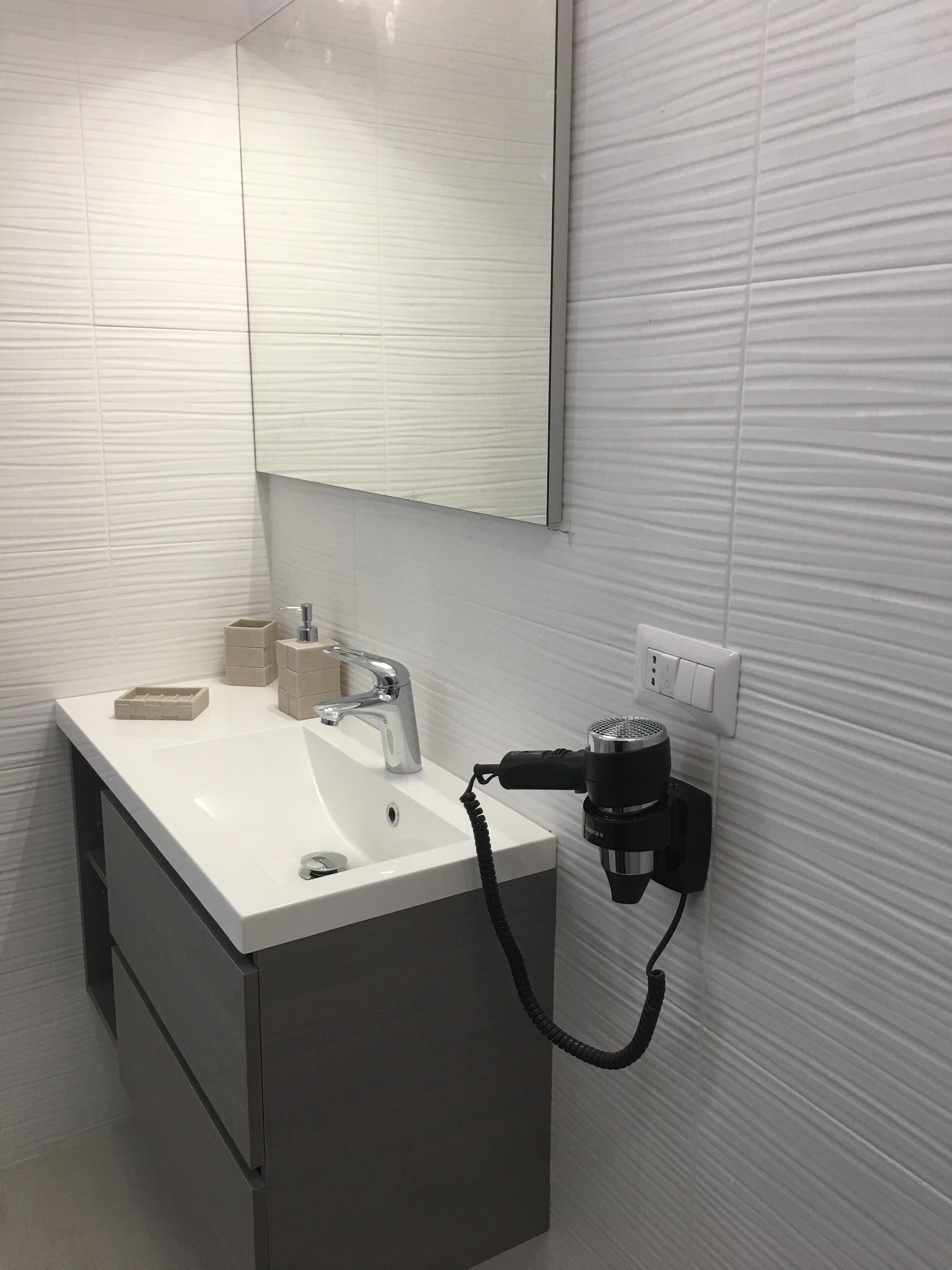 A bathroom with a white sink, a mirror, and a hairdryer plugged into a wall outlet.