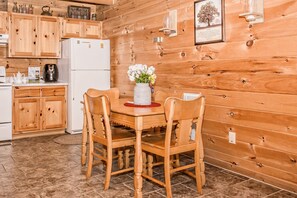 Una cocina con paneles de madera, una mesa de comedor y sillas, un refrigerador y diversos electrodomésticos.