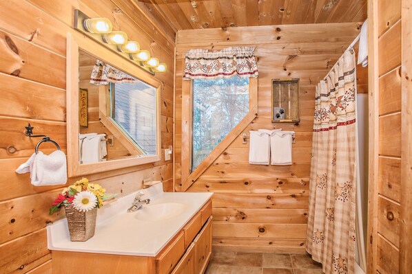 A wooden cabin bathroom with a large mirror, a sink, and a window.