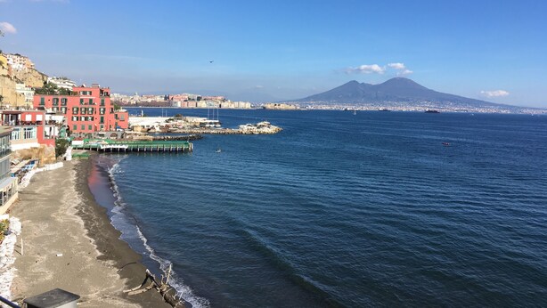 A coastal town with buildings along the beach, a dock, and a mountain in the background. - Casa Nocelle Suite, Boutique and Luxury tiny apartment in the heart of Naples (Napoli)