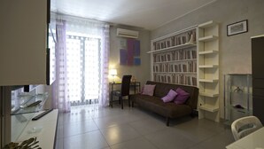 A living room with a sofa, a bookshelf, a desk with a lamp, and a dining area. - Casa Nocelle Suite, Boutique and Luxury tiny apartment in the heart of Naples (Napoli)