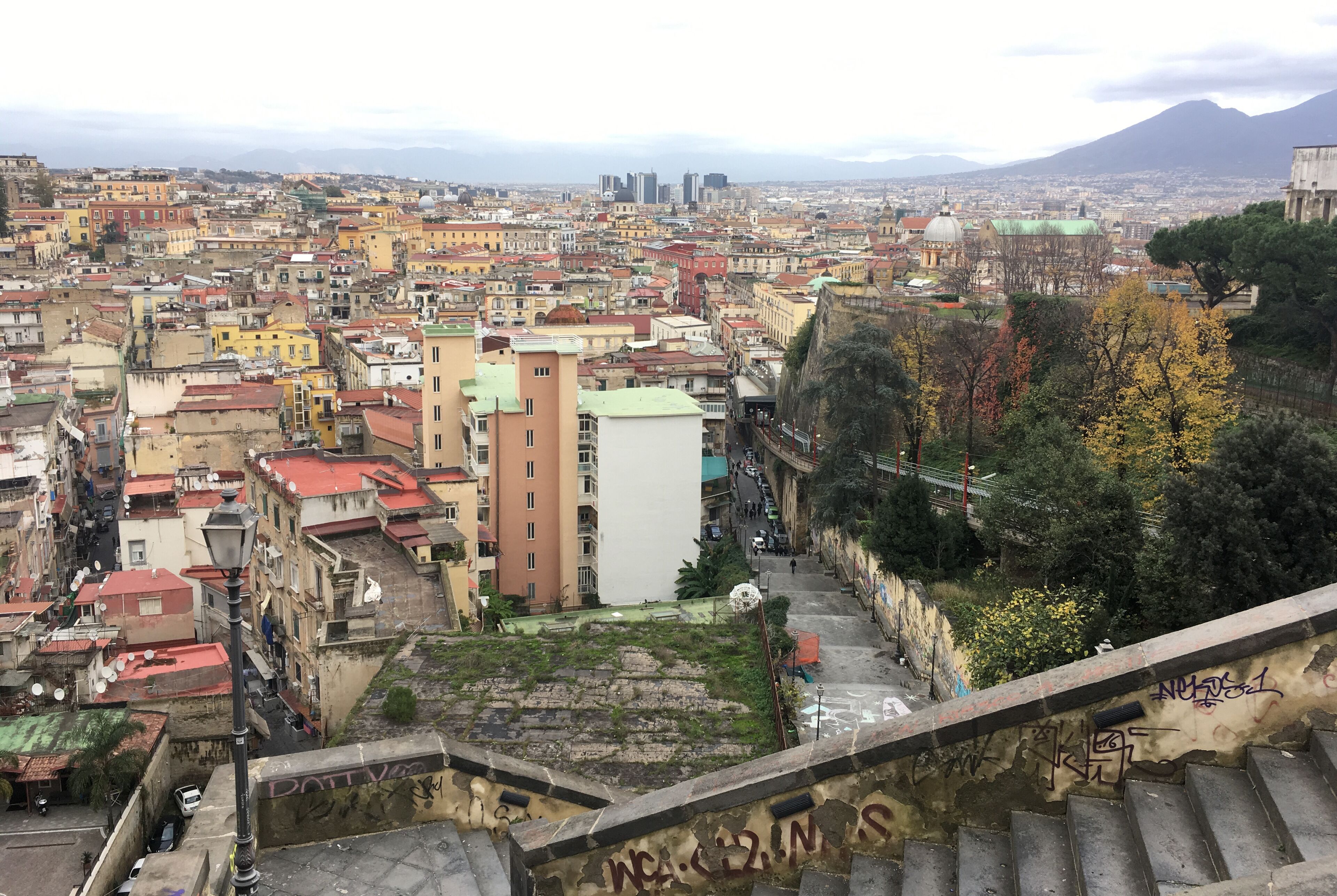 Un paysage urbain mêlant bâtiments historiques et modernes, avec une imposante structure en forme de dôme et un escalier descendant vers une rue.