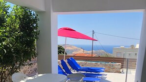 Eine Terrasse mit Tisch und Stühlen, einer Korbschaukel und einem roten Sonnenschirm.
